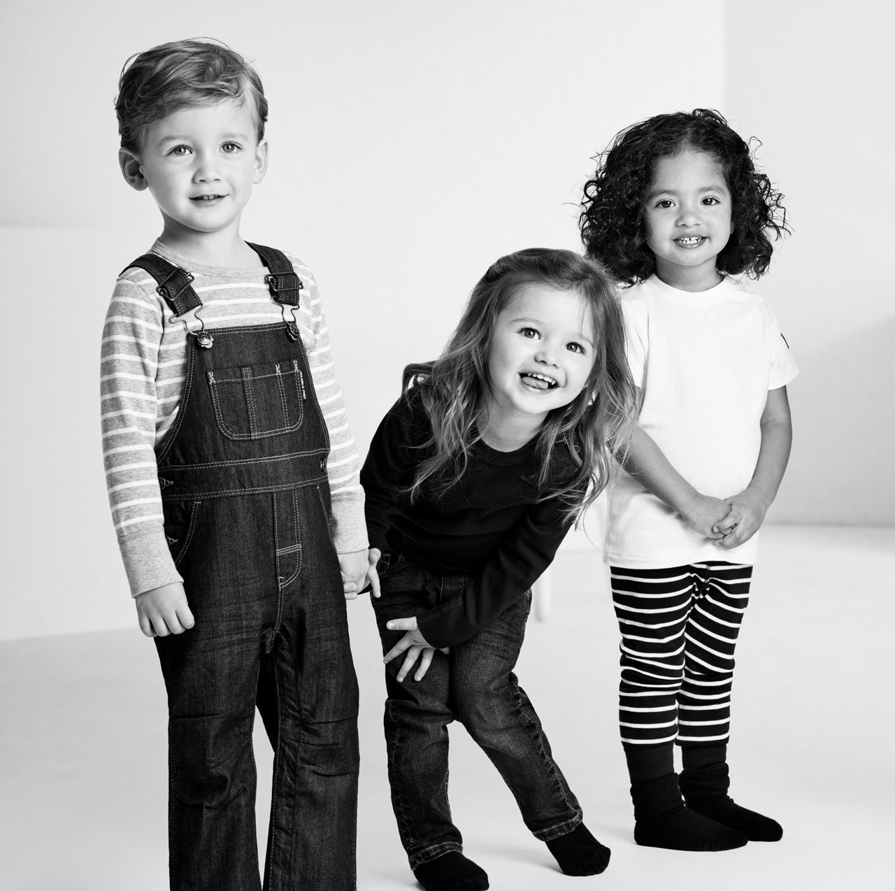 Black-and-white image of three children of varying heights standing and wearing Polarn O. Pyret kids clothing 