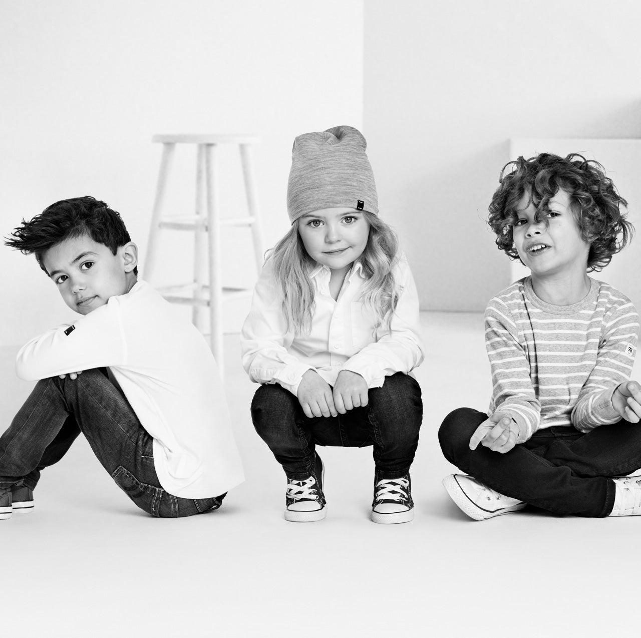 Black-and-white image of three children sitting and wearing Polarn O. Pyret kids clothing 